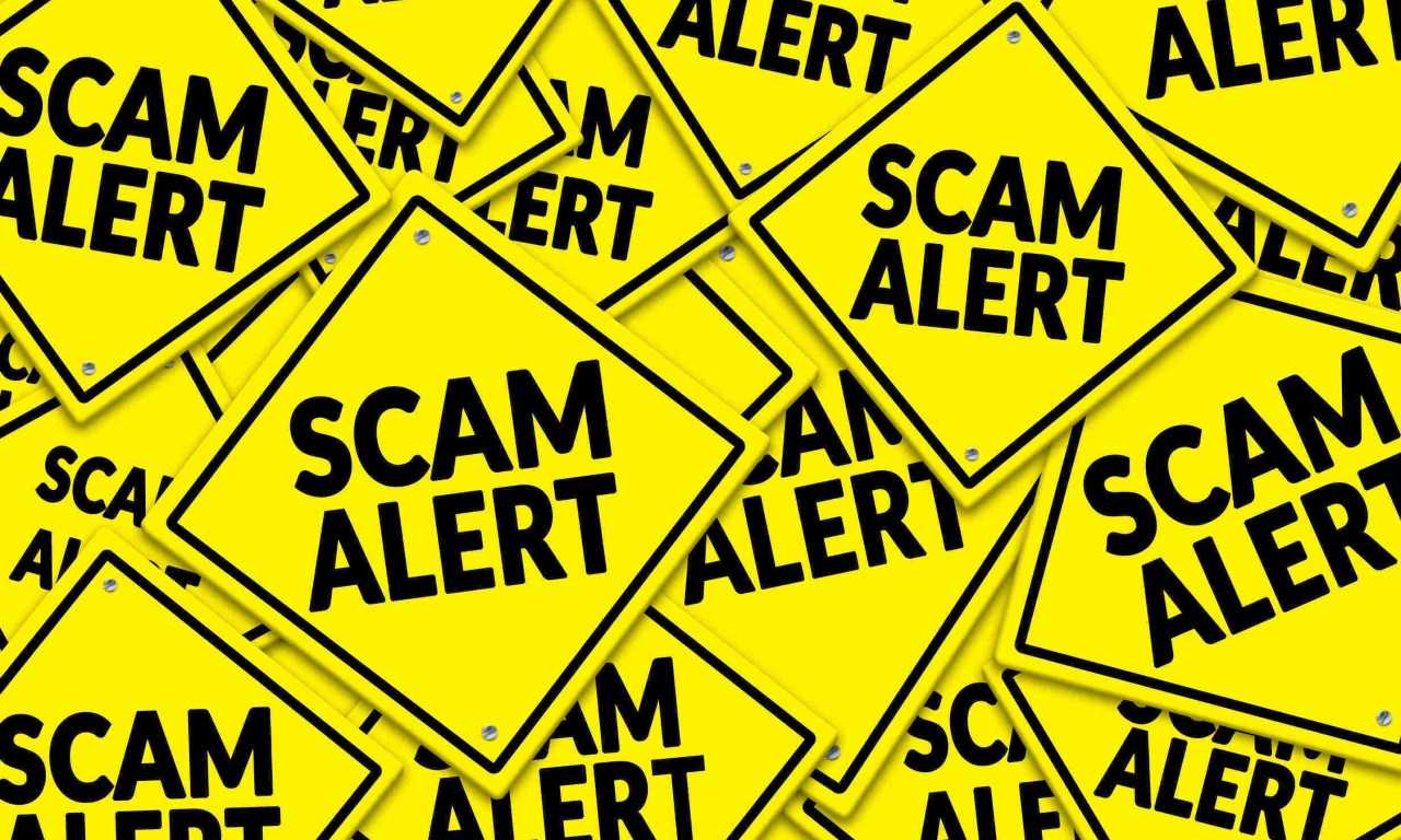 The words “scam alert” on multiple yellow road signs, as a warning to avoid trading scams